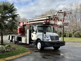 A 2010 International 4300 truck equipped with an aerial lift feature and a flatbed, parked on a street with a palm tree nearby