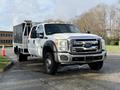 A white 2015 Ford F-550 truck with a flatbed and a tool box mounted in the back is parked on a driveway