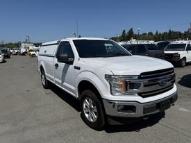 A white 2019 Ford F-150 with a truck bed cover parked in a lot with other vehicles in the background