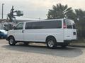 A white 2021 Chevrolet Express van is parked with its side facing the viewer showcasing its large windows and chrome wheels