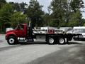 A red 2011 International 4400 truck with a flatbed and black exhaust stack parked at an angle showing the driver's side and cargo area