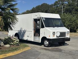 A white 2012 Ford E-450 delivery truck with an open side door and a covered wheel well parked on the street