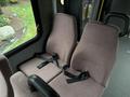 Two beige fabric seats with black seat belts inside a vehicle