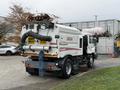 A 2009 UD Trucks UD 3300 street sweeper with a large brush attachment and suction hoses at the rear showcasing a white and red color scheme