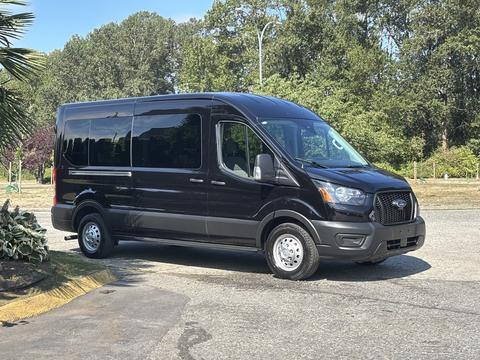 A black 2025 Ford Transit T-350 van with a spacious body and large windows is parked with its front slightly turned toward the viewer