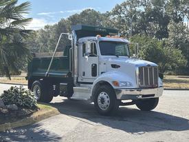 A 2015 Peterbilt 337 dump truck with a shiny silver front and green dump bed parked at an angle with its bed raised