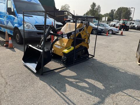 A yellow 2025 AGT MX-MZT14 Mini Loader with a bucket attachment is parked on a concrete surface surrounded by various vehicles and traffic cones