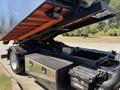 A 2016 Isuzu NPR-HD truck with a tilted bed revealing the undercarriage and storage compartments beneath the chassis