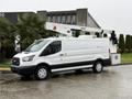 A 2019 Ford Transit utility van equipped with a hydraulic lift and exterior storage compartments parked on a wet surface