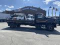 A 1996 GMC Top Kick flatbed truck with a black exterior and a striped design parked with machinery loaded on its bed