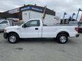 A white 2013 Ford F-150 truck with a flatbed and a ladder rack, positioned side view with chrome wheels