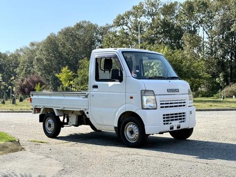 A white 2008 Suzuki Carry pickup truck with a compact design and open cargo bed, featuring a simple front grille and a two-door cab