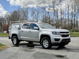 A silver 2018 Chevrolet Colorado pickup truck with a ladder rack on the bed parked on a wet surface