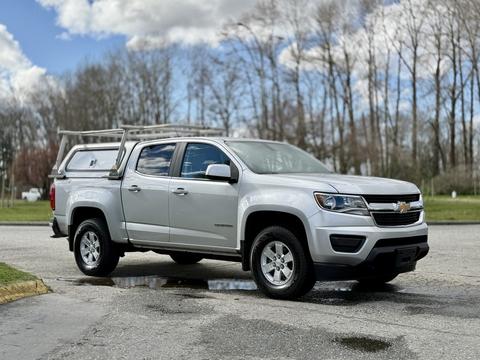 A silver 2018 Chevrolet Colorado pickup truck with a ladder rack on the bed parked on a wet surface