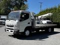 A 2013 Mitsubishi Fuso FE160 truck with a flatbed and a mounted lift mechanism on the back