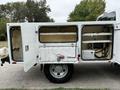 A 2015 Ford F-350 SD with a utility bed featuring a storage compartment with double doors opened showing interior shelving and equipment connections