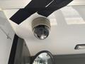 A round black and white surveillance camera mounted on a ceiling with dark straps securing it in place