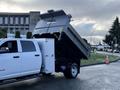 A white 2021 RAM 5500 dump truck with its bed raised and dumping a load retains a boxy design and features a dual rear wheel setup