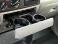 A gray cup holder is open in the dashboard of a 2006 Ford F-550 with controls and knobs above it