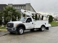 A white 2012 Ford F-450 SD truck with a bucket lift attached in the cargo area designed for utility work