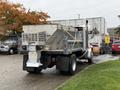 A 2003 Freightliner FL70 dump truck with a gray bed and yellow straps securing its contents