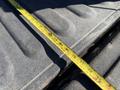 A yellow measuring tape laid across a textured truck bed surface showing the measurement of the truck's cargo area