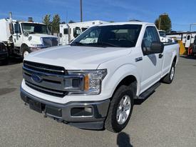 A white 2018 Ford F-150 pickup truck with a chrome grille and silver trim parked in a lot with visible wheels and a bed cover