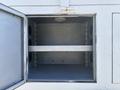 An empty storage compartment of a 2005 Freightliner M2 106 with a metal interior and a horizontal shelf