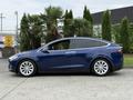A blue 2020 Tesla Model X parked with its distinctive falcon-wing doors closed and sleek design showcased from the side
