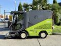 A 2015 Tennant 636 Green Machine compact street sweeper with a gray and green exterior features a large front brush and enclosed cab