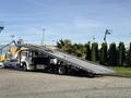 A 2022 Freightliner M2 106 flatbed truck with a lowered ramp is parked on a street