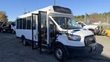 A white 2021 Ford Transit bus with large windows and a door open at the front showing the interior and steps leading inside