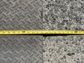 A measuring tape laid across two surfaces one textured metal and the other concrete
