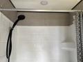 A shower area with white tiled walls a silver showerhead mounted on a pipe and a gray and white patterned shower curtain