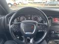 A black 2015 Dodge Charger steering wheel with buttons for audio and cruise control visible along with the instrument cluster displaying speed and other gauges