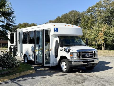 A white 2015 Ford Econoline bus with side doors open and a wheelchair accessibility symbol on the front