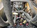 A 2018 John Deere 350 construction machine with numerous pipes and hoses visible above a clutter of discarded containers and debris in the engine compartment