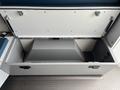 A gray storage compartment with a hinged lid opened, featuring a geometric interior and metal fasteners inside a 2020 Mercedes-Benz Sprinter 2500