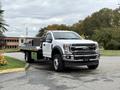 A 2022 Ford F600 flatbed truck with a white exterior and black cargo area parked at an angle showcasing its front and side profile