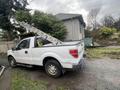 A white 2011 Ford F-150 pickup truck with a ladder rack in the truck bed is parked on a gravel area