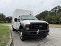 A 2008 Ford F-450 Super Duty truck with a white box body in the foreground featuring a black grille and bright orange lights on the roof