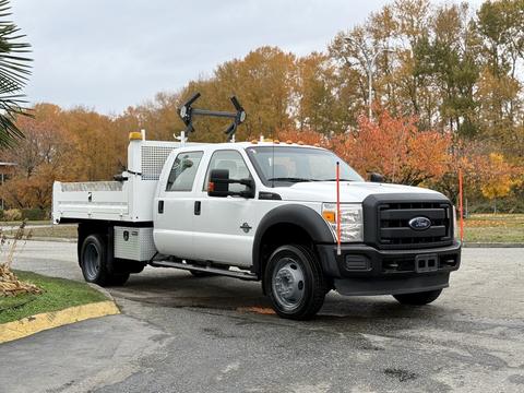 A 2013 Ford F-550 truck with a white exterior and flatbed design featuring side tool storage and equipment mounts on the roof