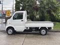 A white 2010 Suzuki Carry mini truck with a flatbed, featuring a compact design and small wheels, parked on a concrete surface