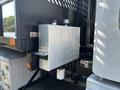 A metallic rectangular tank mounted on the side of a 2020 Peterbilt 330 truck with various fittings and a latch visible on the surface