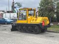 A yellow 2004 Bombardier SW48 with tank tracks and a snowplow attachment is parked on a paved surface