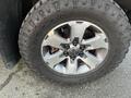 Close-up of a silver alloy wheel from a 2014 Ford F-150 featuring five spokes and rugged all-terrain tires with visible tread wear