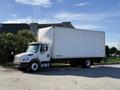 A white 2012 Freightliner M2 106 box truck parked at an angle with a large cargo area and a front cab featuring a prominent grille and headlights