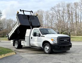 A 2015 Ford F-350 dump truck with a white exterior lifting its black dump bed at an angle