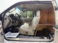 Inside a 2008 Ford F-450 SD the driver's side features a beige leather seat with a wooden partition behind it creating a divided space