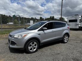 A silver 2015 Ford Escape displayed in a parking area with an open driver side door and visible alloy wheels